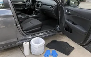 Open left-hand-drive car door with paper towels, gloves, and floor mat on driveway