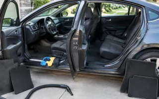 Open car doors with floor mats removed and cleaning tools on the driveway sill