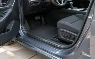 Open driver door on a paved driveway with crumbs along the sill and floor mat