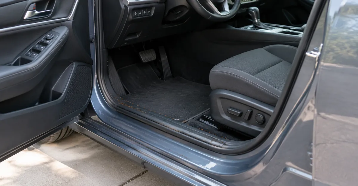 Open driver door on a paved driveway with crumbs and debris along the sill and floor mat edge