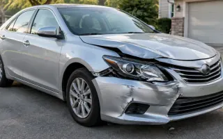 Sedan with front-end damage parked on a U.S. residential driveway, still upright and intact enough to roll